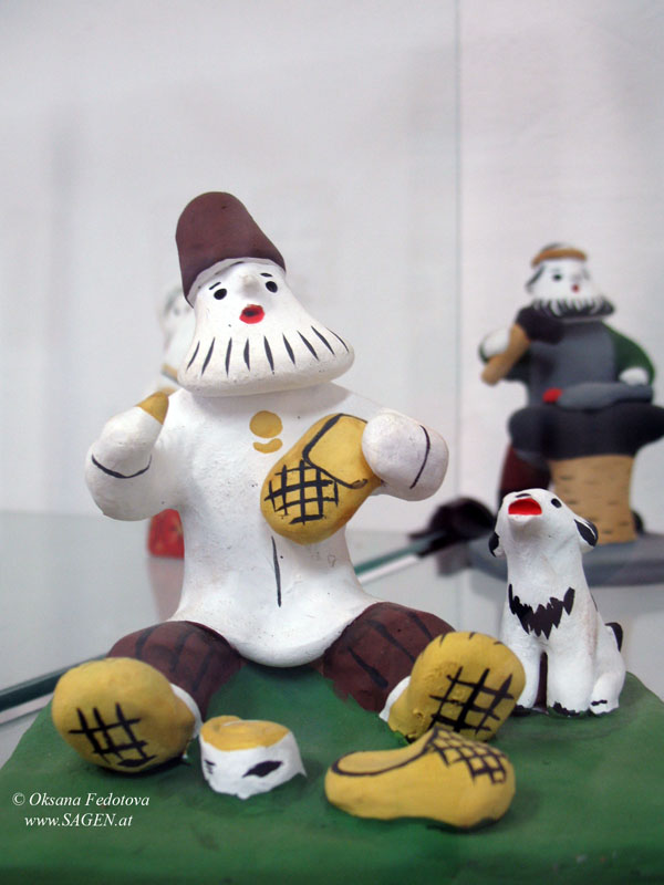 Mann bei der Anfertigung von Bastschuhen („Lapti“). Im Hintergrund – ein Eisenschmied. Museum des Kargopoler Spielzeuges im Zentrum der Volkshandwerke „Bereginja“. Kargopol © Oksana Fedotova 